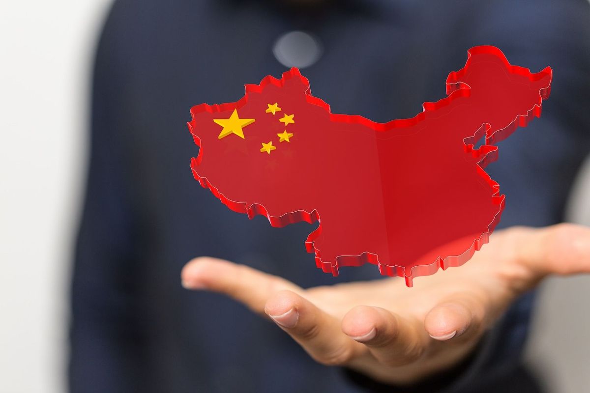 Hand holding a 3D map of China, colored in red with yellow stars.